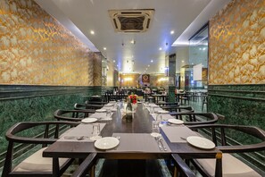 A restaurant with a long table set for dining, marble walls, and a chandelier. - Foxoso Hotel Delhi Airport (New Delhi)
