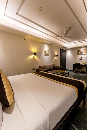 A hotel room with a large bed, a sofa, a desk, and a ceiling fan. - Foxoso Hotel Delhi Airport (New Delhi)