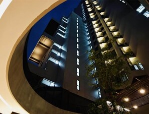 A modern building with multiple floors, illuminated windows, and a circular architectural feature.