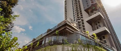 A high-rise building with a balcony and greenery, labeled 'THE AYOMA.'