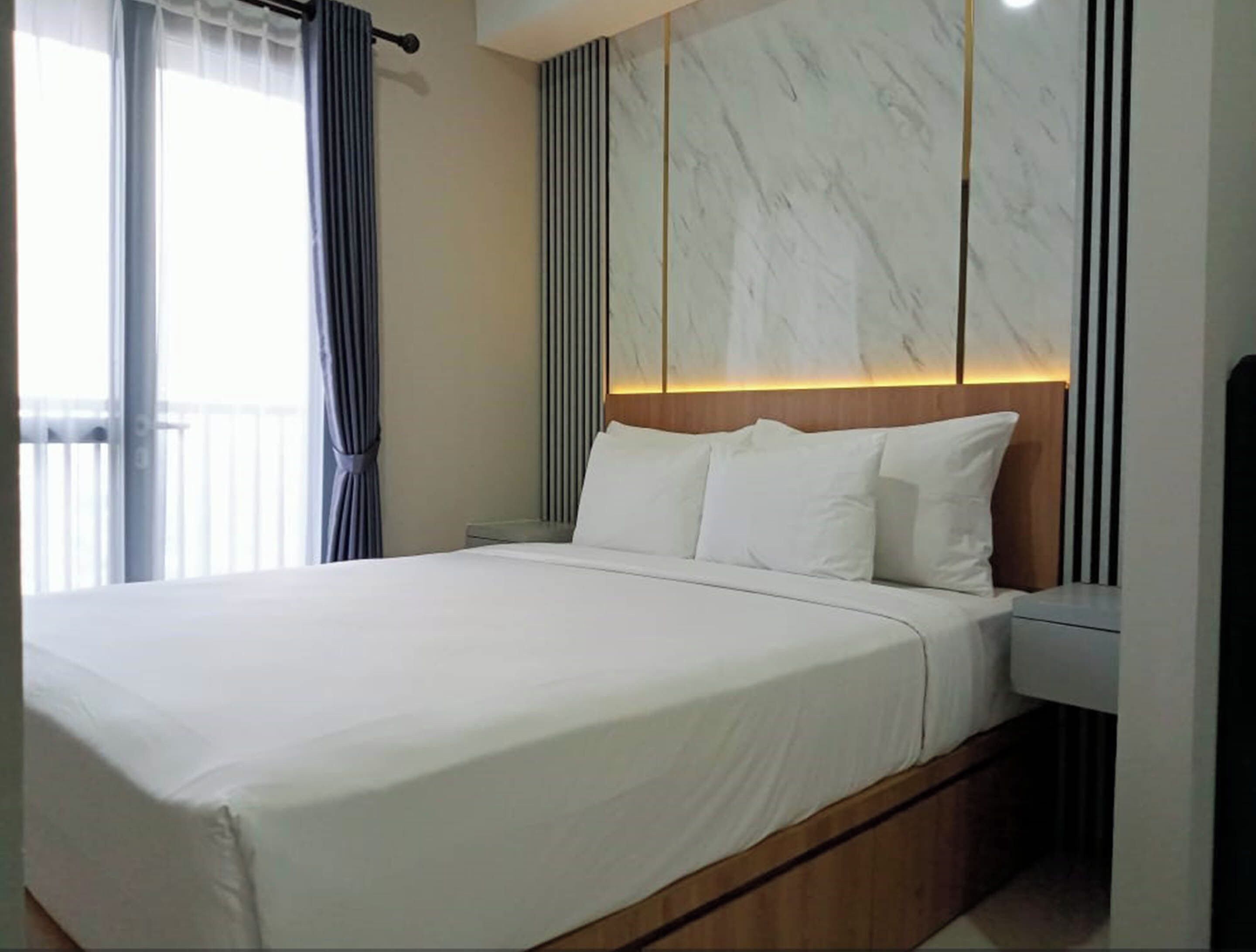 A modern hotel room with a large bed, a wooden headboard, and a marble accent wall.