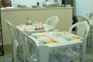 Un comedor con sillas y mesas de plástico blanco, cada juego con platos, cubiertos y cristalería.