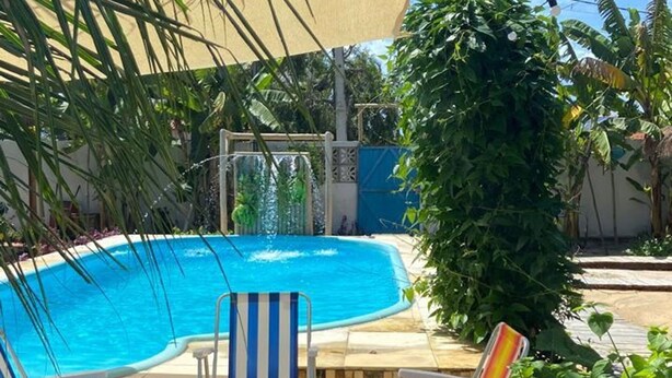 A swimming pool with lounge chairs, a shaded area, and surrounding greenery. - Pousada Vila Lua Bela (Pitimbu)