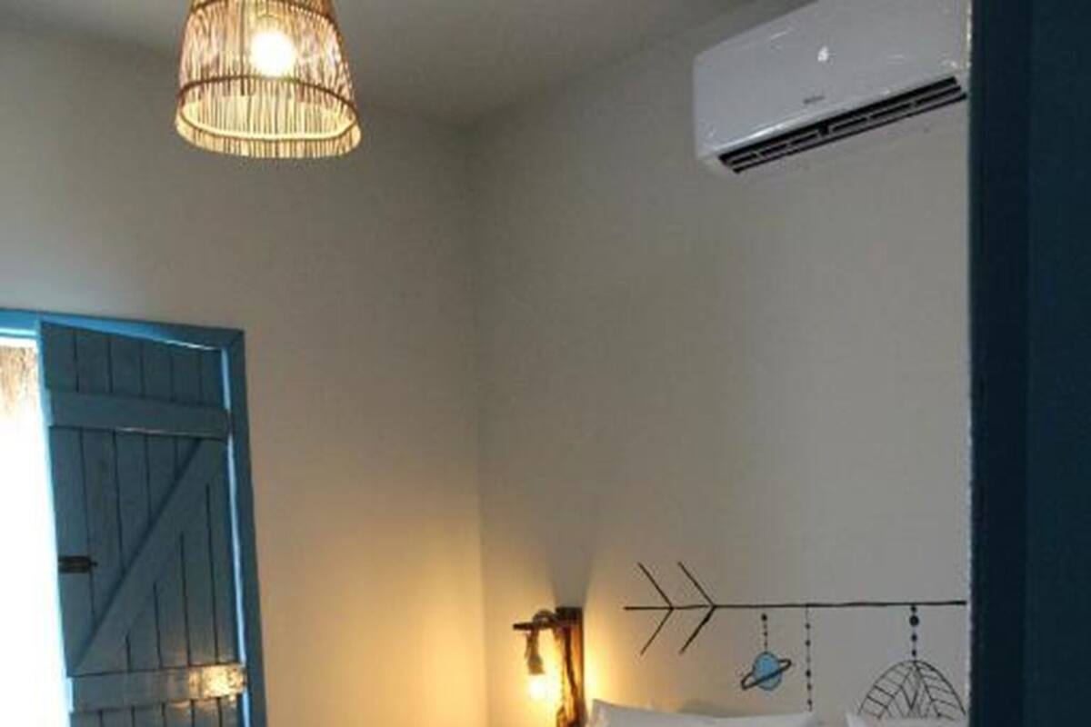 Un dormitorio con cama, aire acondicionado de pared, una lámpara decorativa en la pared y una puerta azul.