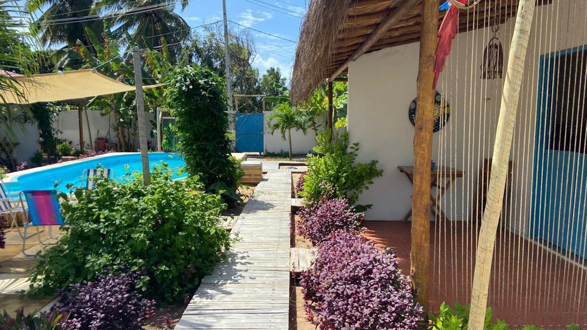 A pool area with a wooden deck, surrounded by lush greenery and a thatched-roof structure.