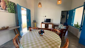 A dining area with a round table, chairs, a television, and a blue door. - Pousada Vila Lua Bela (Pitimbu)