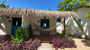 A thatched-roof building with two doors, a hammock, and a pathway leading to it. - Pousada Vila Lua Bela (Pitimbu)