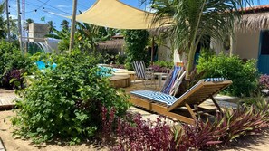 A poolside area with lounge chairs, a table, and a thatched-roof building. - Pousada Vila Lua Bela (Pitimbu)