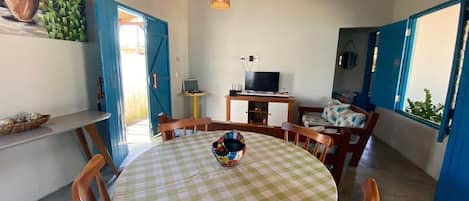 A dining area with a round table, chairs, a television, and a blue door.