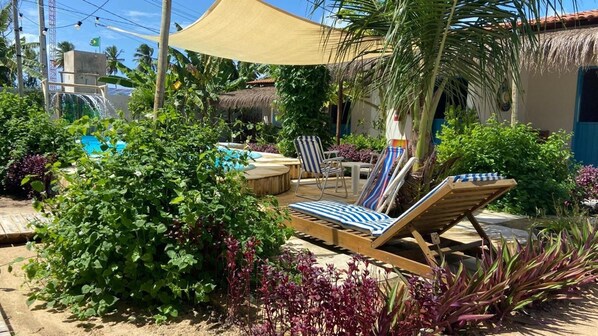 A poolside area with lounge chairs, a table, and a thatched-roof building.