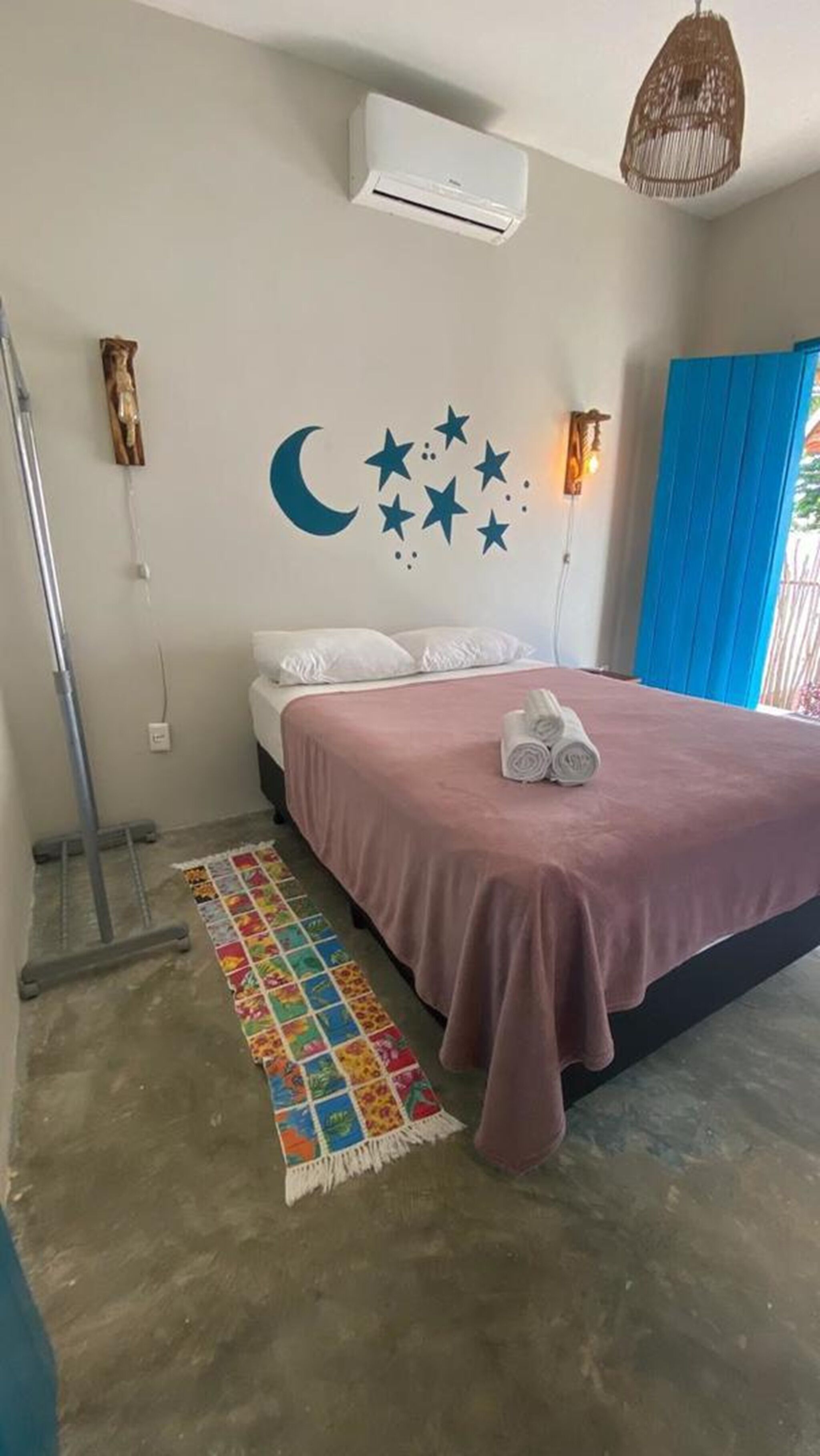 A bedroom with a bed, a wall-mounted air conditioner, a wall decoration of stars and a crescent moon, a colorful rug, and a blue curtain.