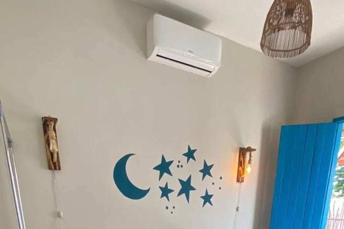 Un dormitorio con una cama, un aire acondicionado de pared, una decoración de estrellas y luna creciente, una alfombra colorida y una cortina azul.