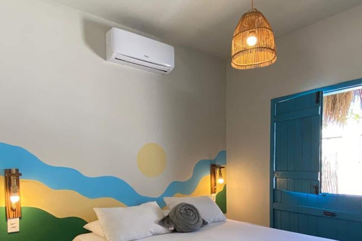 Un dormitorio con cama, aire acondicionado, lámpara colgante y un mural en la pared.