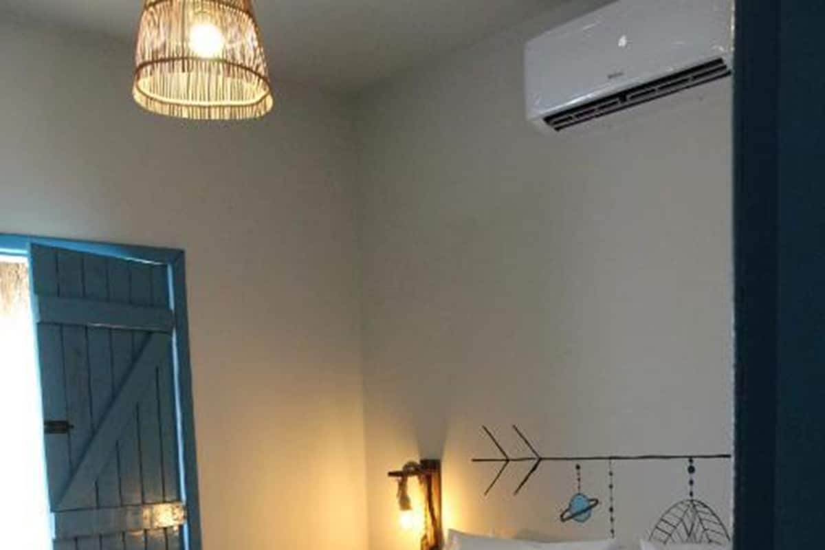 A bedroom with a bed, a wall-mounted air conditioner, a decorative wall light, and a blue door.