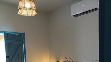 Quarto com cama, ar condicionado fixado na parede, luminária decorativa e porta azul.
