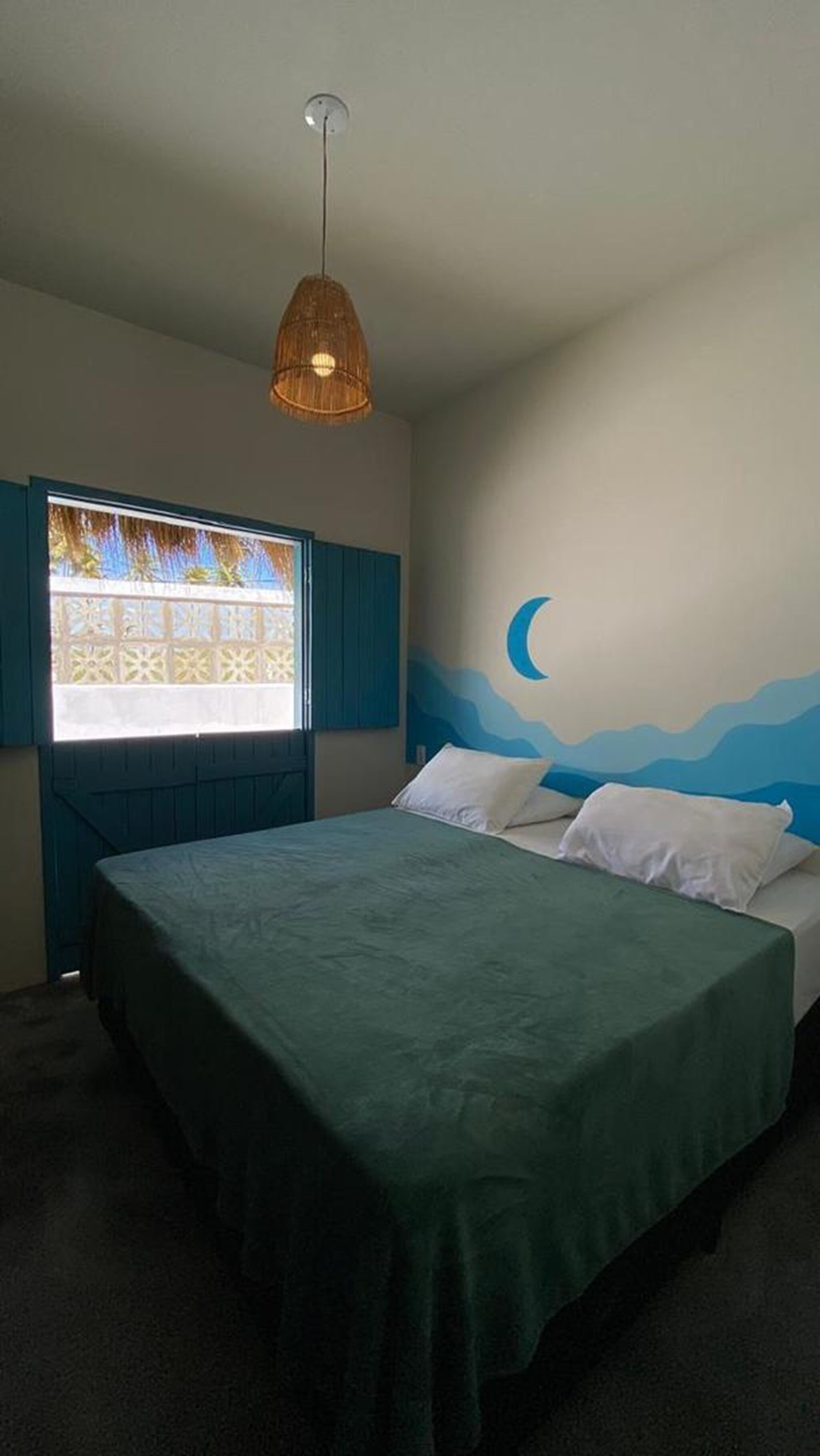 A bedroom with a bed, a window with a view, a wall mural, and a hanging light fixture.