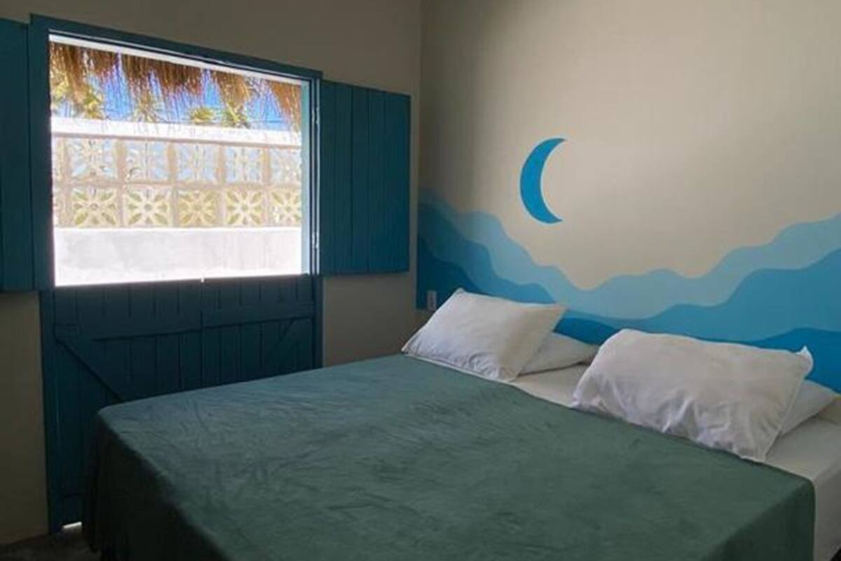 Un dormitorio con cama, ventana con vistas, un mural en la pared y una lámpara colgante.