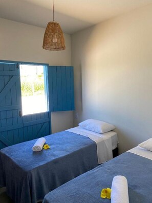 Una habitación con dos camas, una puerta azul y una lámpara colgante.