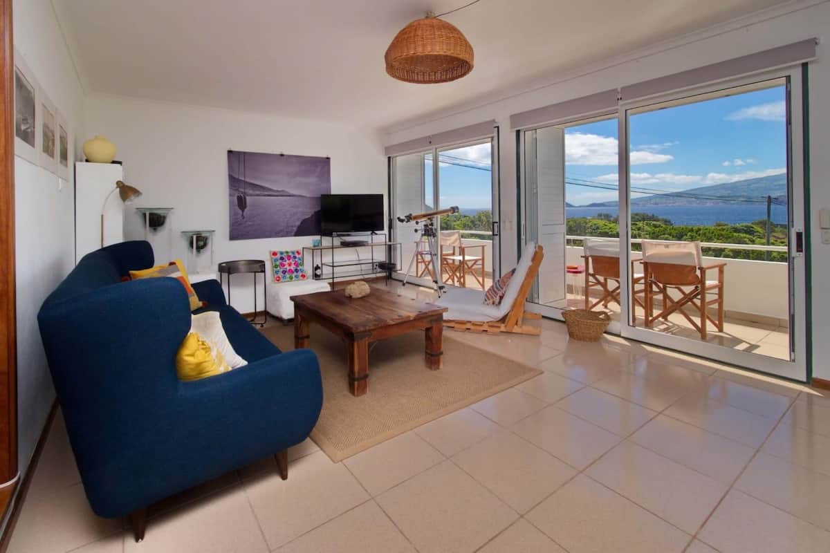 Una sala de estar con sofá, una mesa de centro, televisor y un balcón con vistas.