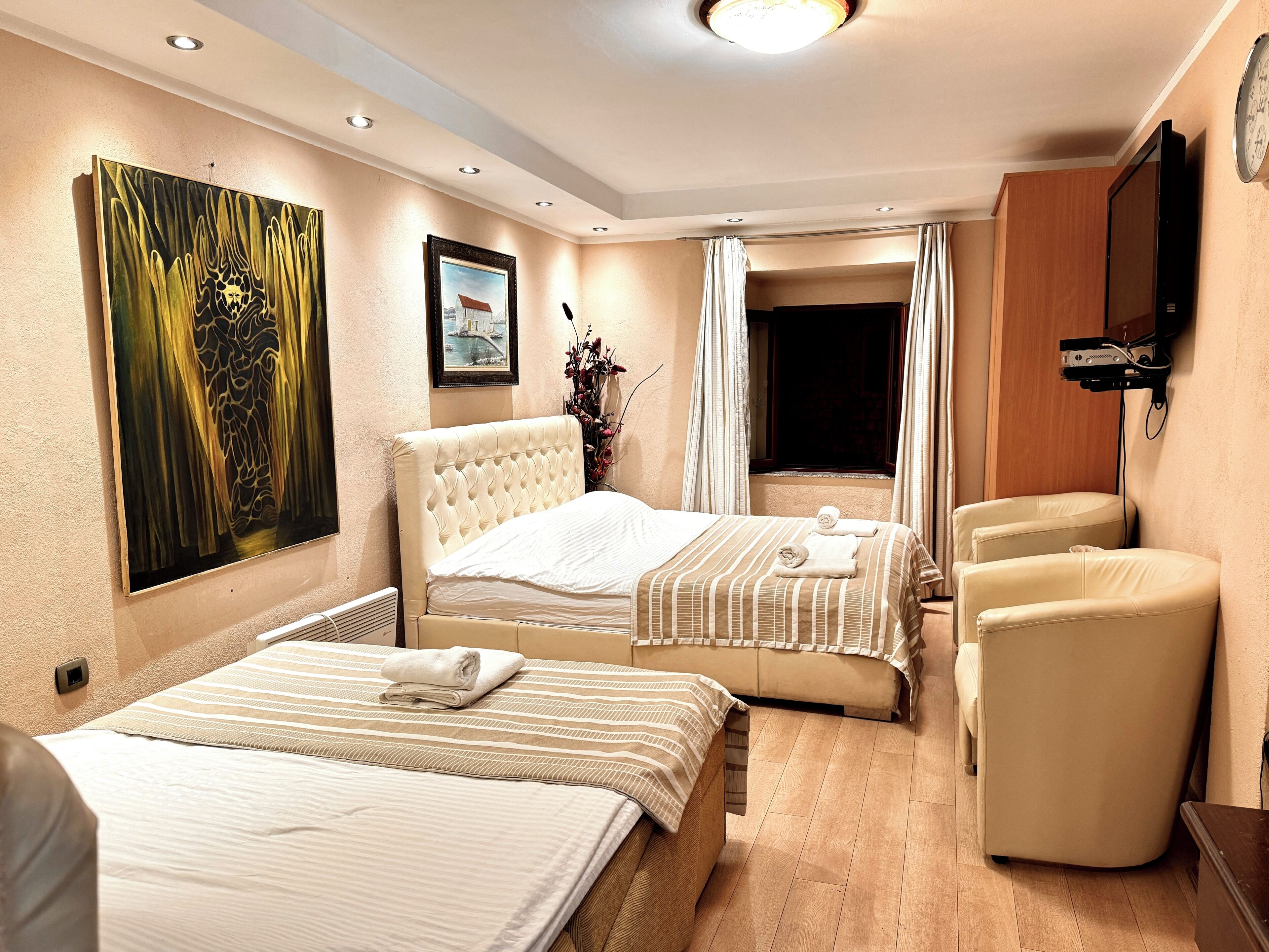 A hotel room with two beds, a TV, a chair, and artwork on the walls.