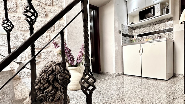 Eine Treppe mit aufwendiger Metallreling, ein Küchenbereich mit weißen Schränken und ein Granitboden.