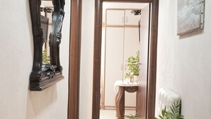 Ein Flur mit einem Spiegel, einem Blumentopf, einem kleinen Tisch mit einer Pflanze und einer Tür zu einem Zimmer.