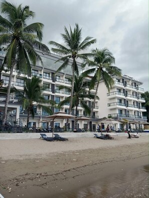 A beachfront hotel with multiple floors, palm trees, and outdoor seating areas. - Angel Garden Resort (Busuanga)