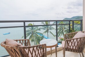 A balcony with wicker chairs, a small round table, and a view of the sea with palm trees and a boat. - Angel Garden Resort (Busuanga)