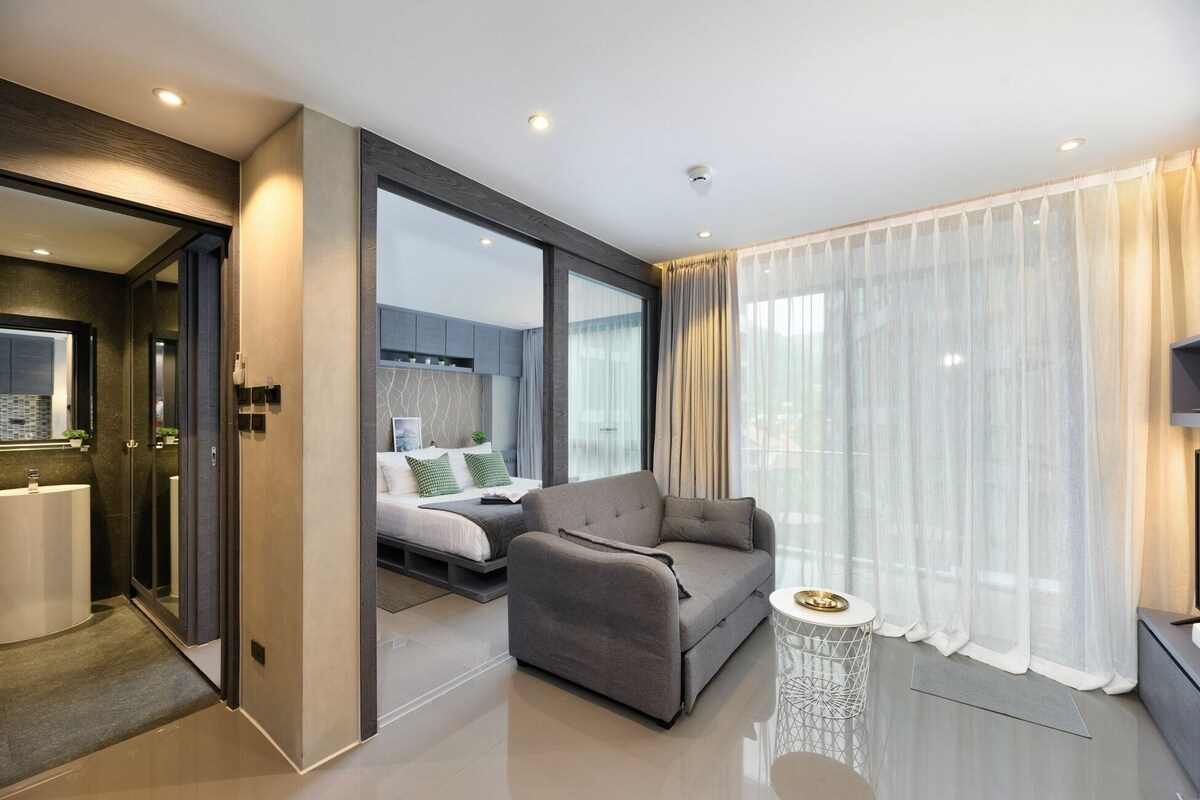 Ein modernes Hotelzimmer mit einer Couch, einem kleinen Beistelltisch, einem Bett mit Blick und einem Badezimmer mit Spiegel und Waschbecken.