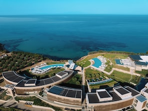 An aerial view of a resort with a large swimming pool, multiple guest rooms, and a view of the sea. - Zelia Halkidiki (Nea Propontida)