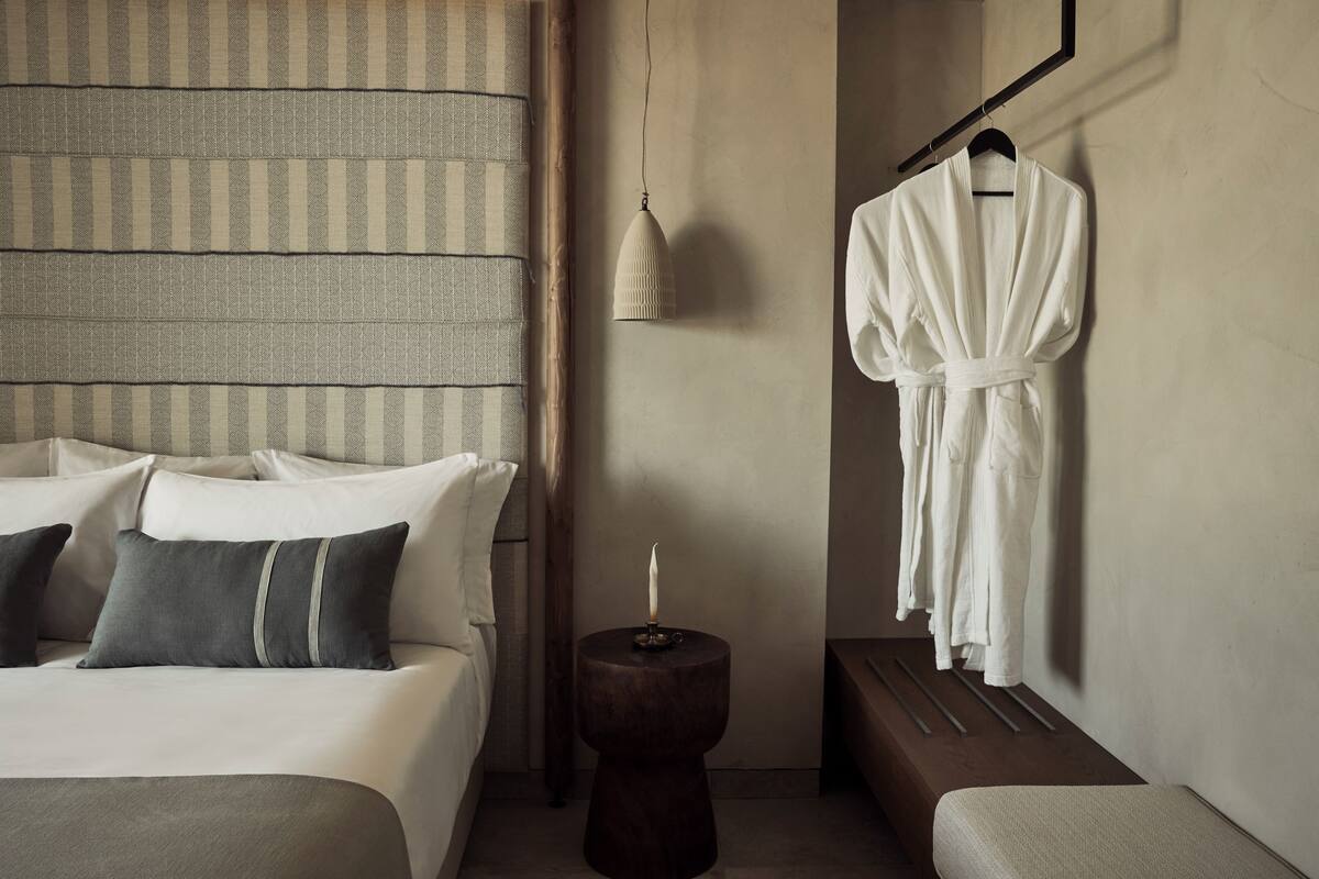 Una habitación de hotel con cama, mesita de noche, bata colgada y una lámpara fijada a la pared.