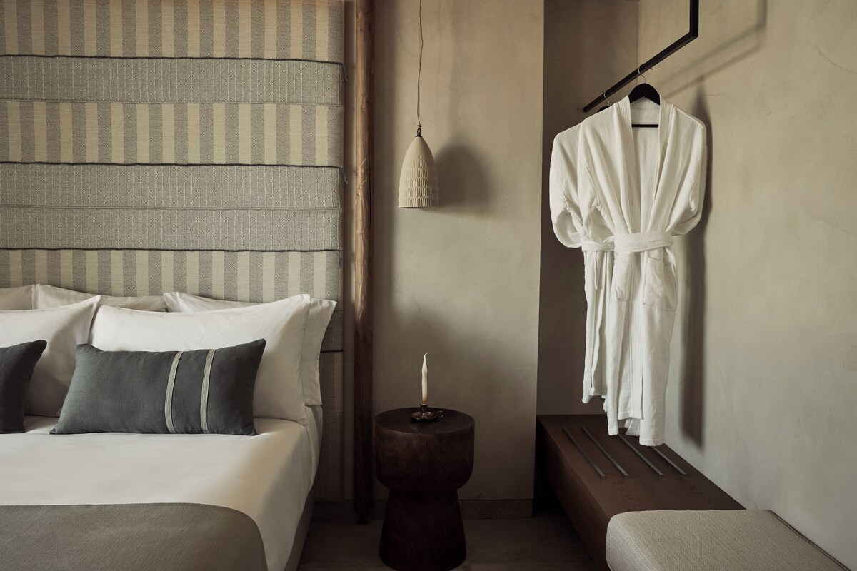 A hotel room with a bed, bedside table, robe hanging, and a wall-mounted lamp.