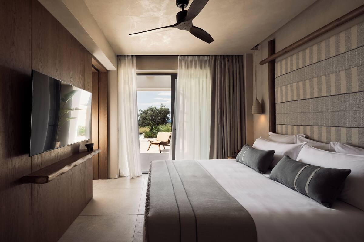 Habitación de hotel moderna con una cama grande, televisor de pantalla plana, ventilador de techo y vistas al exterior.