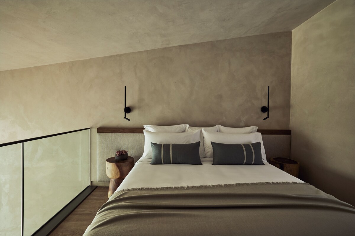A bedroom with a bed, bedside tables, a nightstand, and a view of the balcony.