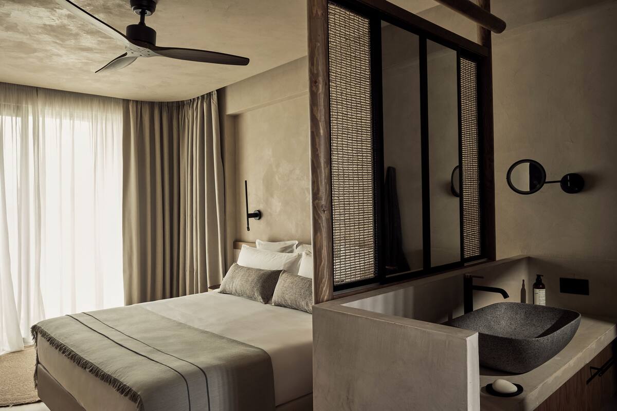 Una habitación de hotel moderna con una cama grande, un lavamanos empotrado y un ventilador de techo.