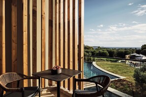 A wooden balcony with a table and chairs, overlooking a swimming pool and a landscaped garden. - Zelia Halkidiki (Nea Propontida)