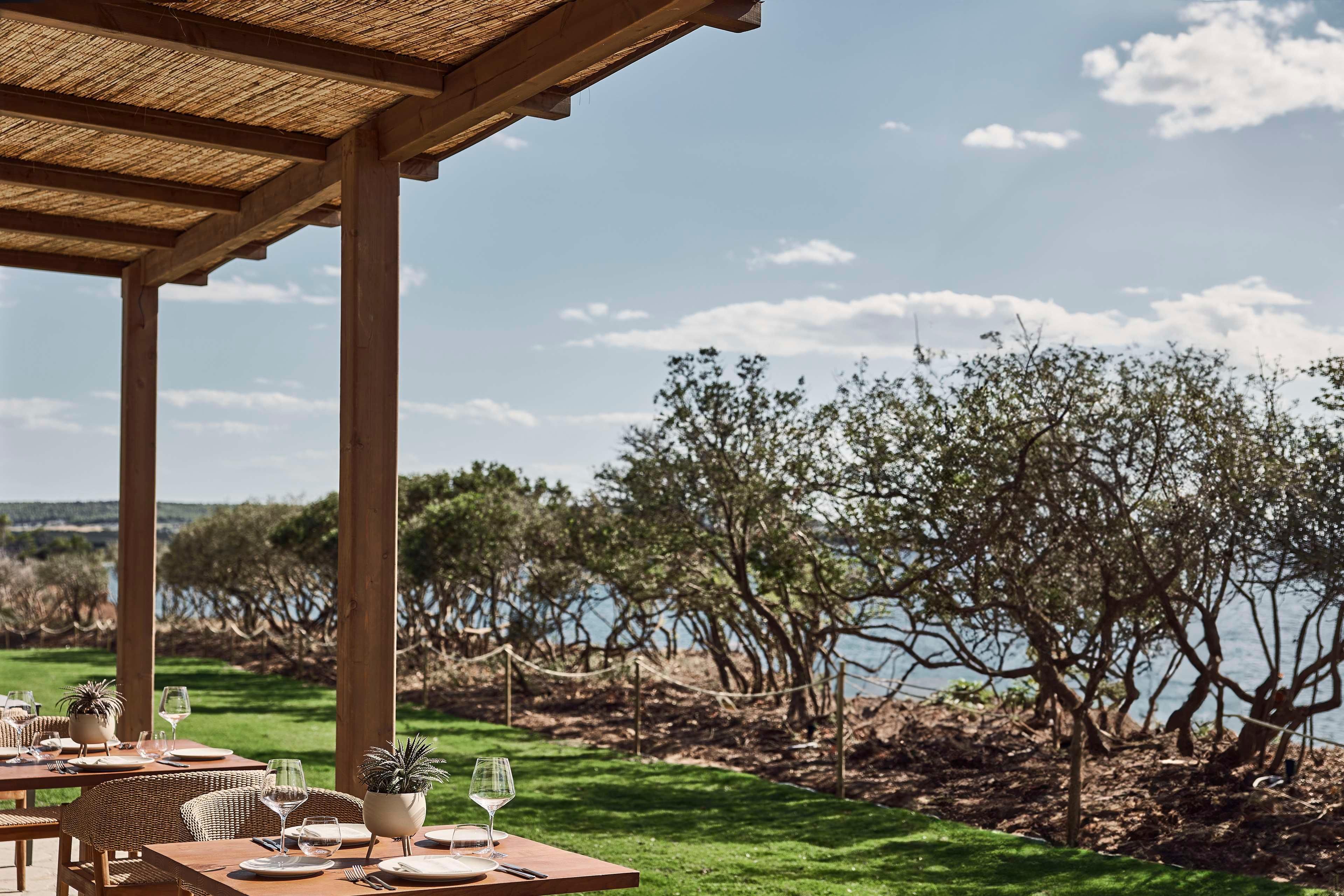 An outdoor dining area with tables set for two, overlooking a body of water and trees.