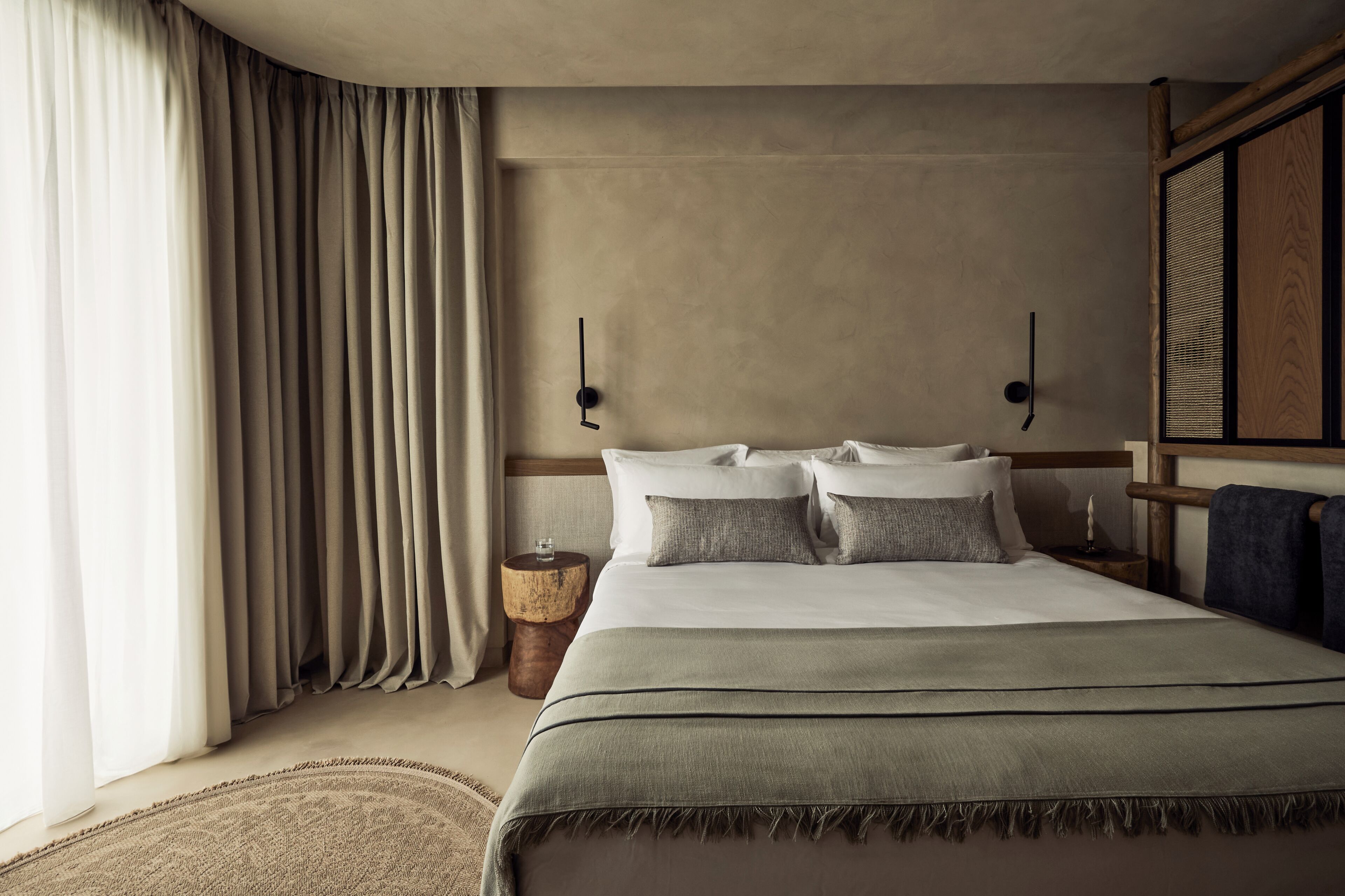 A hotel room with a bed, curtains, a bedside table, and a wall-mounted clock.