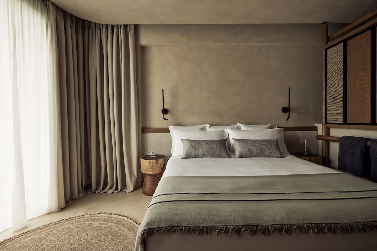 Una habitación de hotel con cama, cortinas, mesita de noche y un reloj en la pared.