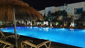 A nighttime swimming pool with lounge chairs and a thatched umbrella. - Hotel Diar Yassine Djerba (Aghir)