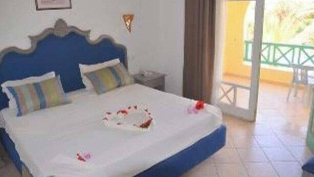 A bedroom with a bed, a nightstand, and a view of the outdoors. - Hotel Diar Yassine Djerba (Aghir)