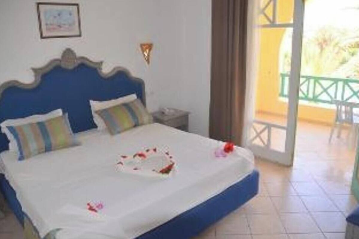 A hotel room with a bed, a nightstand, a framed picture on the wall, and a balcony with a railing.