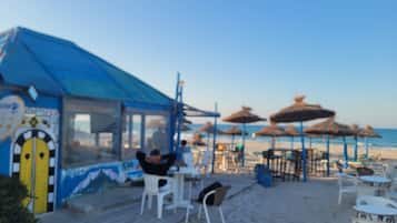 Un cafè a la vora de la platja amb terrassa i una tenda blava.