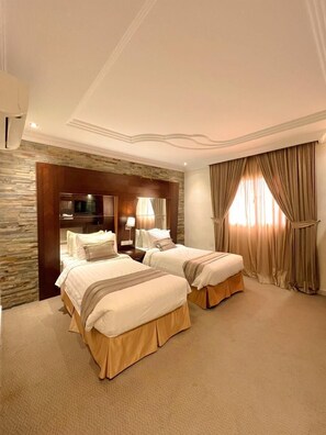A hotel room with two beds, a stone accent wall, a large mirror, and a window with curtains. - Loren Suites (Jeddah)