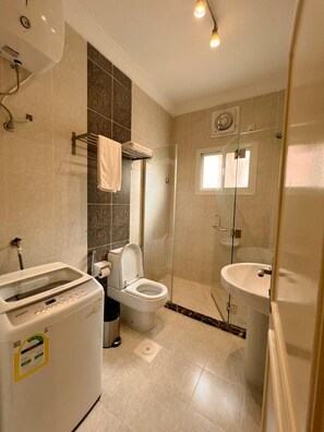A modern bathroom with a shower, toilet, and washing machine. - Loren Suites (Jeddah)