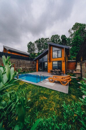 Uma casa moderna com piscina, mobiliário de exterior e uma parede de pedra.