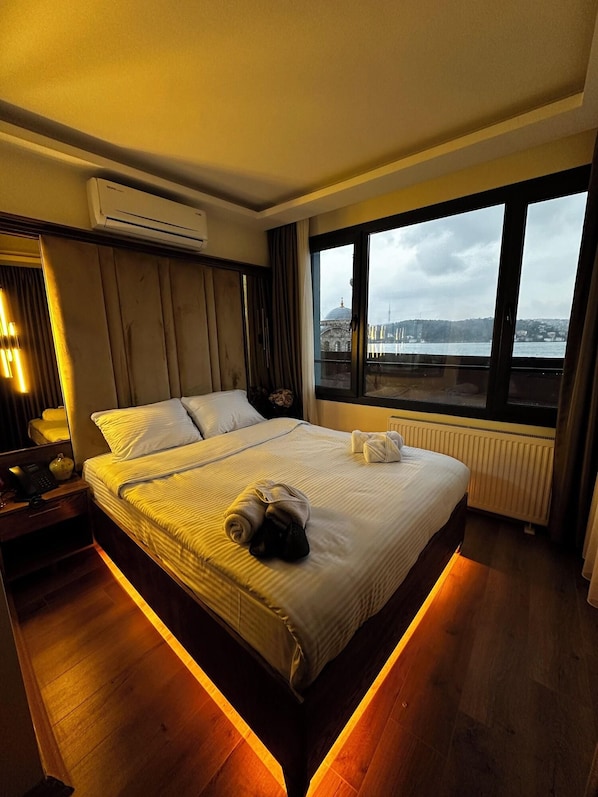 A hotel room with a large bed, a nightstand, a mirror, and a window with a city view. - Lokka Hotel Ortakoy (Istanbul)