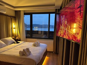 A hotel room with a bed, a large window with a view of a body of water and a distant building, and a wall-mounted TV. - Lokka Hotel Ortakoy (Istanbul)