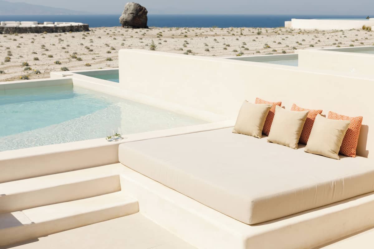 A poolside seating area with steps leading to the water, a view of the beach, and a large rock in the background.