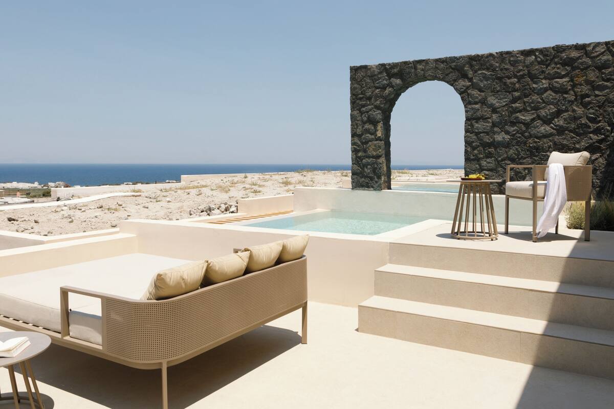 A rooftop terrace with a stone archway, a pool, lounge chairs, and a table with a towel.